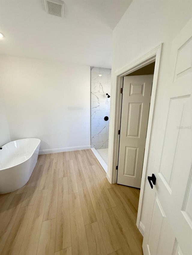 bathroom with a freestanding bath, a marble finish shower, baseboards, wood finished floors, and visible vents