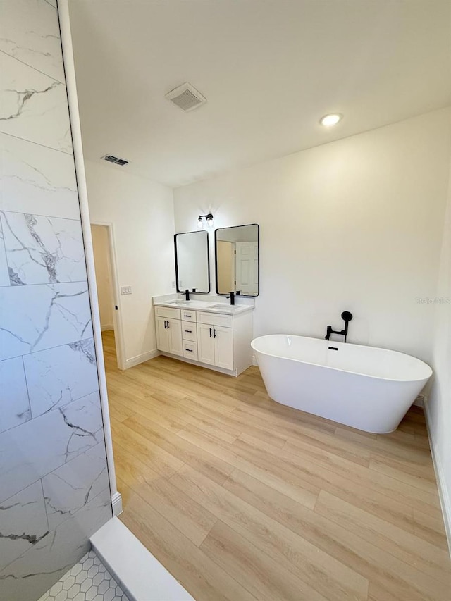 full bathroom featuring double vanity, a freestanding tub, wood finished floors, and visible vents