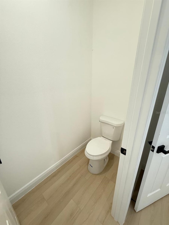 bathroom with toilet, baseboards, and wood finished floors