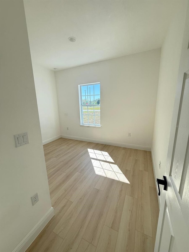 spare room with baseboards and light wood-style floors