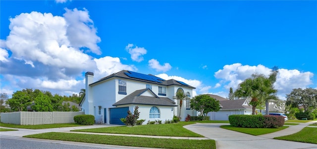 traditional-style home featuring fence, a front lawn, roof mounted solar panels, a chimney, and driveway