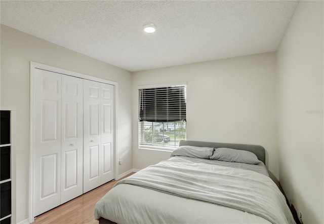 bedroom with a closet, a textured ceiling, light wood finished floors, and baseboards