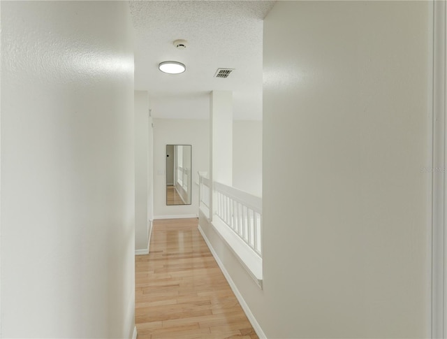 corridor with a textured ceiling, baseboards, visible vents, and light wood-style flooring