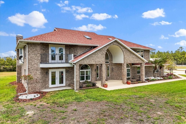 rear view of property with brick siding, a balcony, a yard, and french doors