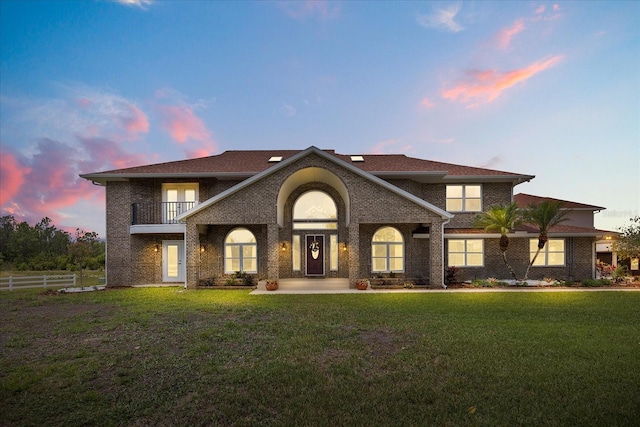 exterior space featuring brick siding, fence, a balcony, and a front yard
