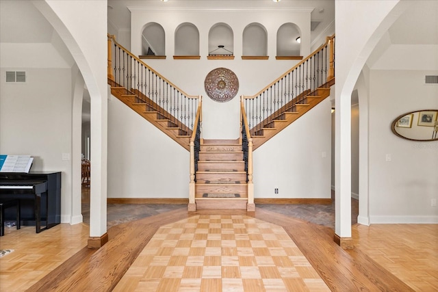 stairway with baseboards, arched walkways, a high ceiling, and visible vents