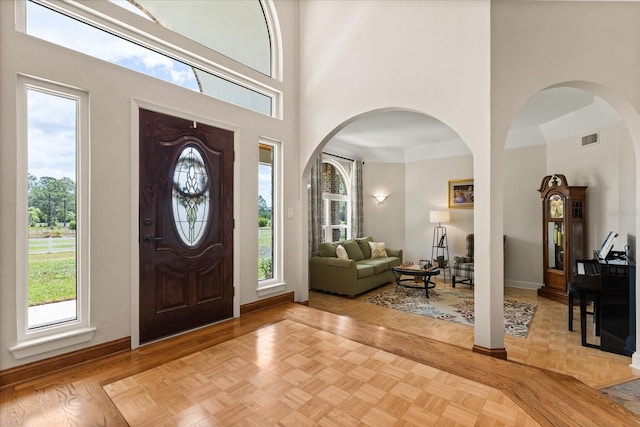 entrance foyer featuring plenty of natural light, arched walkways, baseboards, and a towering ceiling