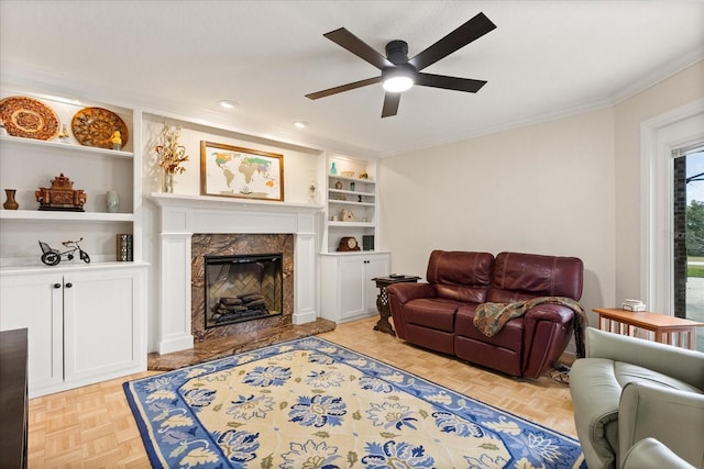 living room featuring a ceiling fan, crown molding, a fireplace, built in shelves, and recessed lighting