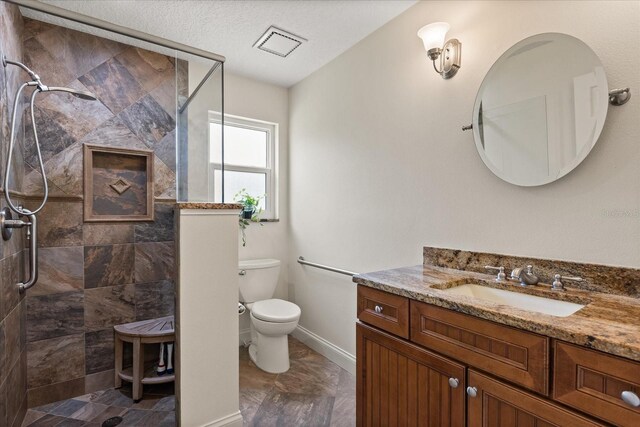 bathroom with vanity, visible vents, toilet, baseboards, and tiled shower
