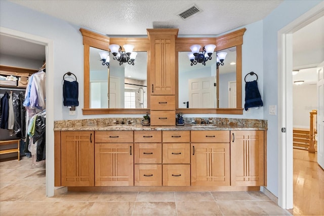 bathroom with double vanity, a notable chandelier, a walk in closet, and visible vents