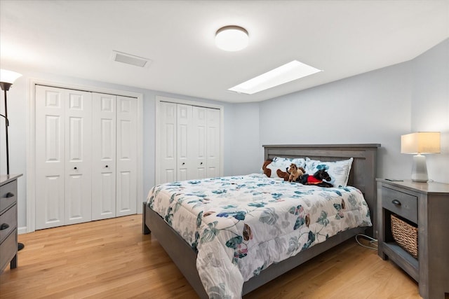bedroom with a skylight, multiple closets, and light wood-style floors