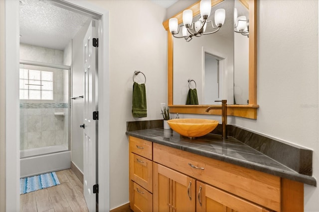 bathroom with a textured ceiling, wood finished floors, vanity, shower / bath combination with glass door, and a notable chandelier