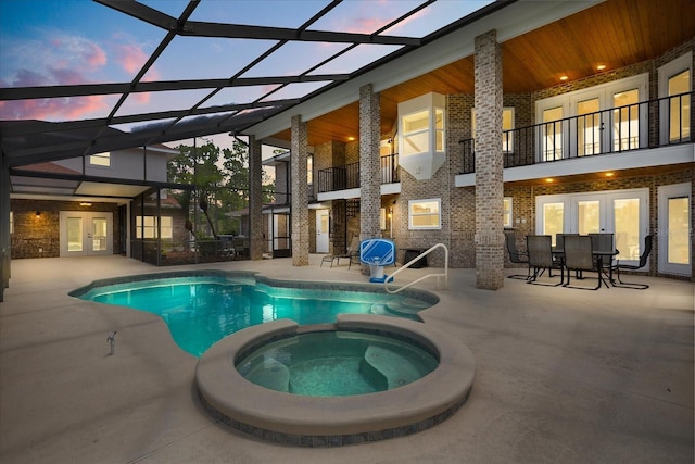 view of swimming pool with french doors, glass enclosure, a pool with connected hot tub, and a patio area