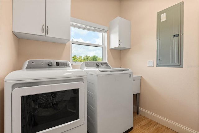laundry area featuring washing machine and dryer, baseboards, light wood-style floors, electric panel, and cabinet space