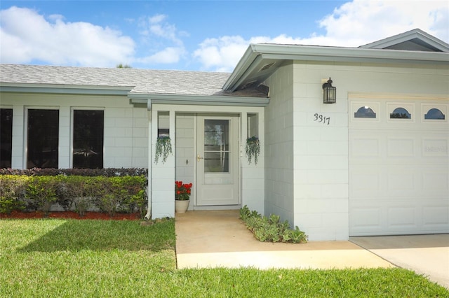 property entrance with a lawn, a garage, concrete block siding, and roof with shingles