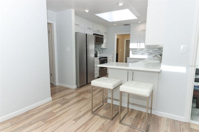 kitchen featuring appliances with stainless steel finishes, a peninsula, decorative backsplash, a kitchen bar, and a skylight