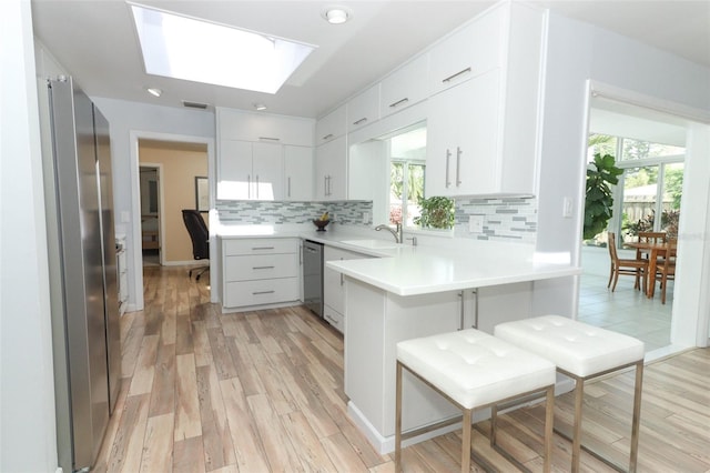 kitchen with a peninsula, a sink, light wood finished floors, backsplash, and stainless steel appliances