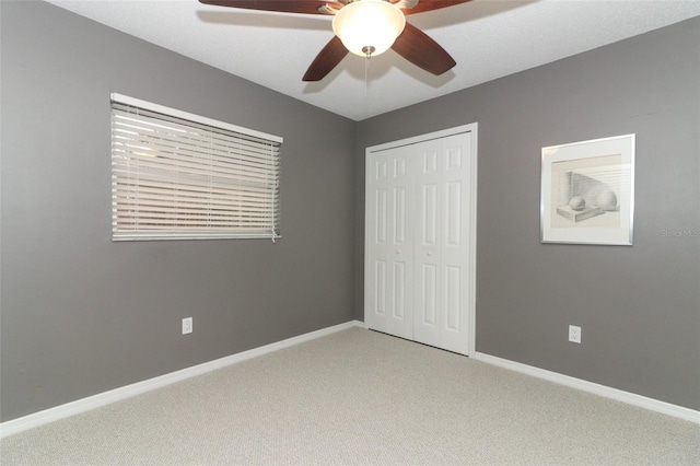unfurnished bedroom featuring baseboards, ceiling fan, a closet, and light colored carpet