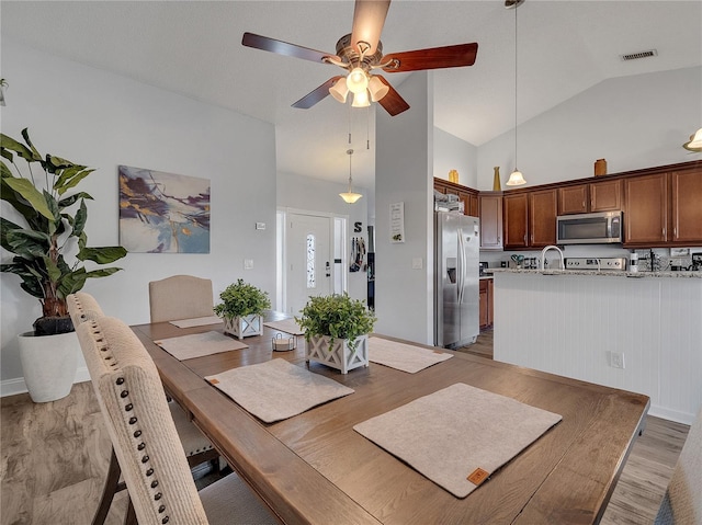 dining area featuring light wood-style floors, high vaulted ceiling, a ceiling fan, and visible vents