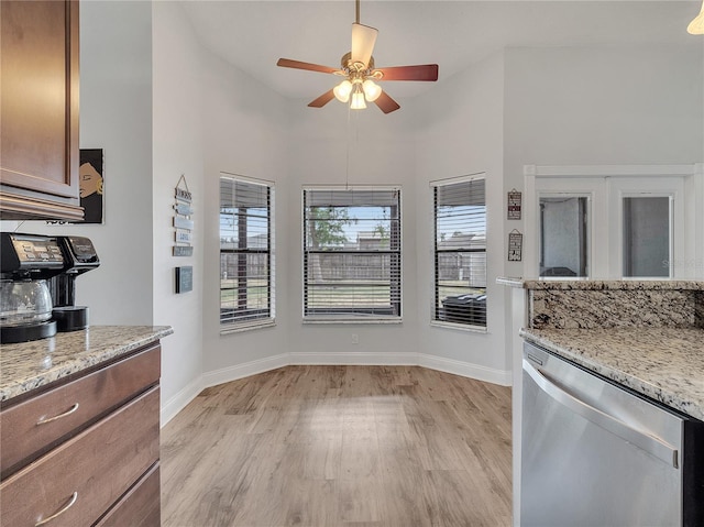 kitchen with a ceiling fan, stainless steel dishwasher, light stone counters, baseboards, and light wood-style floors