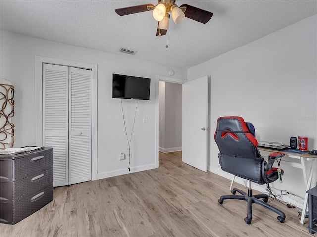 office space featuring light wood-style floors, a textured ceiling, a ceiling fan, baseboards, and visible vents