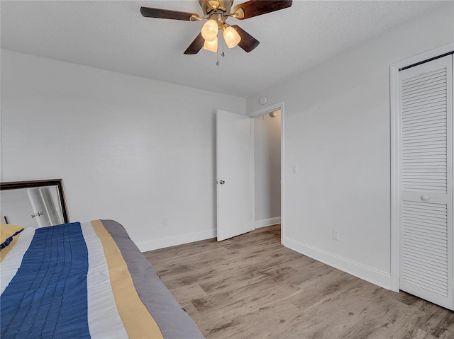 bedroom featuring ceiling fan, a textured ceiling, wood finished floors, baseboards, and a closet