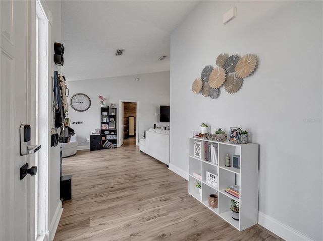 hall with baseboards, visible vents, wood finished floors, and lofted ceiling