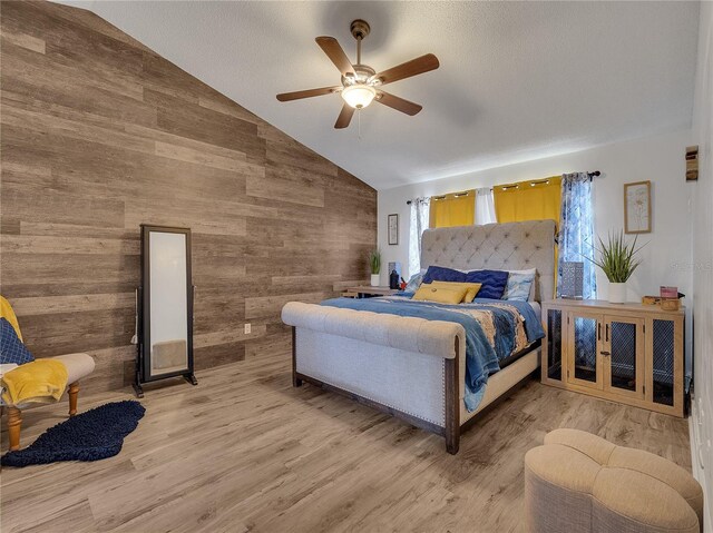 bedroom with wooden walls, high vaulted ceiling, ceiling fan, and light wood-type flooring
