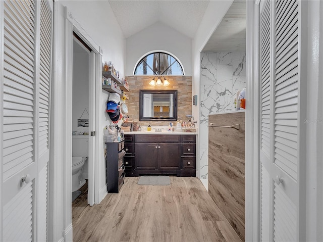 full bath with a closet, vanity, lofted ceiling, wood finished floors, and toilet