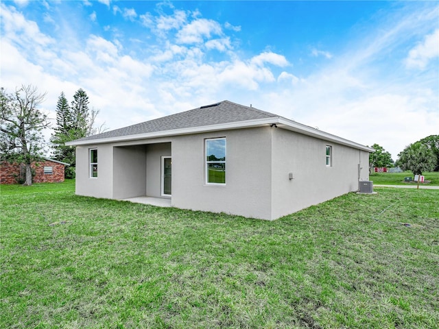 back of property featuring a yard, a shingled roof, stucco siding, and central AC unit