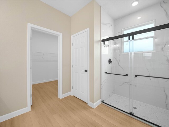 bathroom featuring a marble finish shower, wood finished floors, baseboards, a spacious closet, and recessed lighting