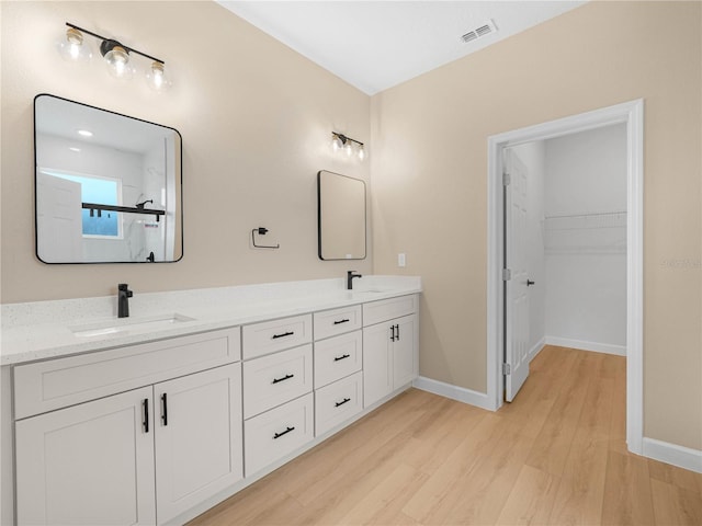 bathroom with wood finished floors, baseboards, double vanity, and a shower