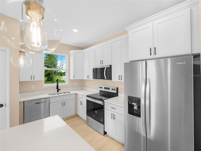 kitchen featuring a sink, stainless steel appliances, white cabinets, light countertops, and light wood-style floors