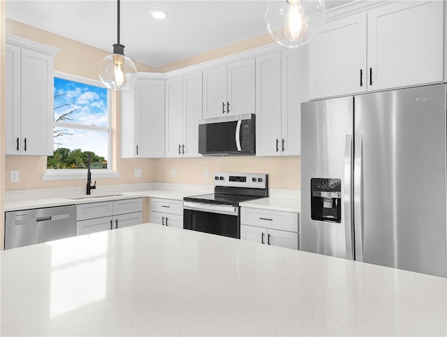 kitchen featuring stainless steel appliances, a sink, white cabinets, recessed lighting, and decorative light fixtures