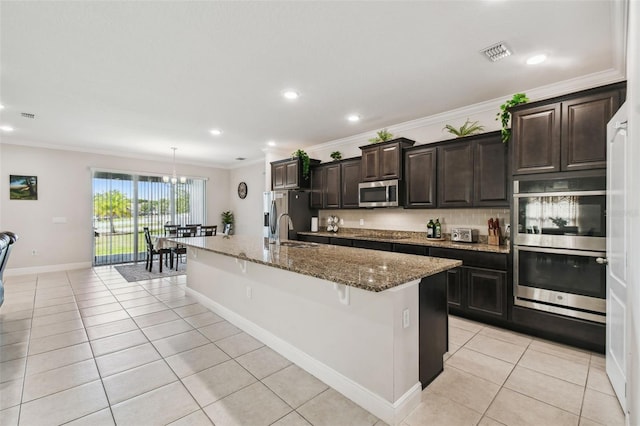 kitchen with light tile patterned flooring, appliances with stainless steel finishes, a sink, visible vents, and a center island with sink