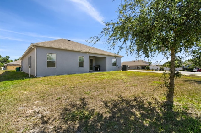 rear view of property with a lawn, central air condition unit, and stucco siding