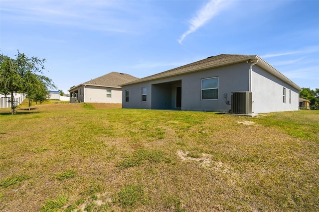rear view of property with central air condition unit, stucco siding, and a yard