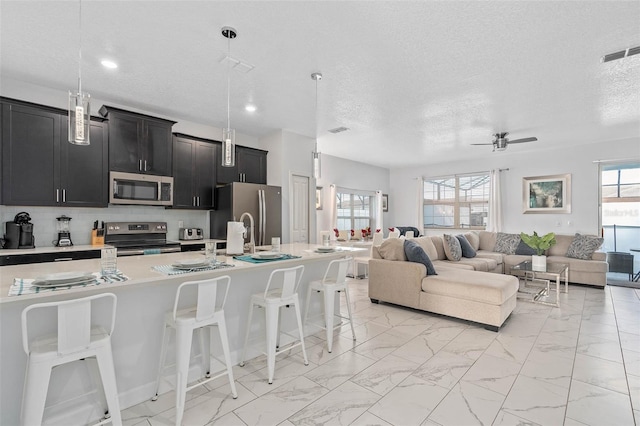kitchen with visible vents, open floor plan, a kitchen breakfast bar, dark cabinets, and stainless steel appliances