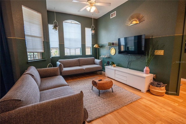 living area featuring a ceiling fan, a textured wall, visible vents, and wood finished floors