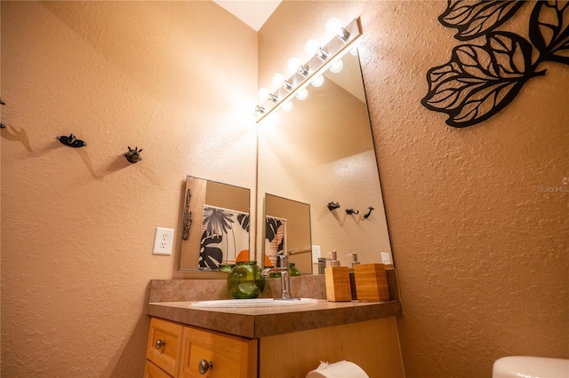 bathroom featuring vanity, a textured wall, and toilet