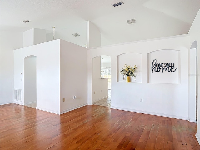 spare room featuring visible vents, arched walkways, wood-type flooring, and high vaulted ceiling