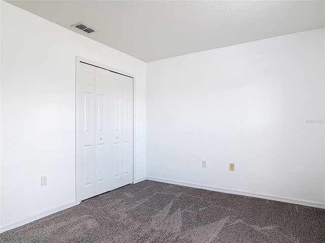 unfurnished bedroom featuring visible vents, baseboards, dark carpet, and a closet