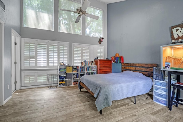 bedroom featuring ceiling fan, visible vents, wood finished floors, and a towering ceiling