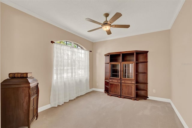 empty room with ceiling fan, light colored carpet, baseboards, and ornamental molding