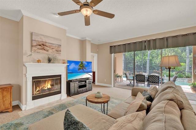 living area with ceiling fan, a textured ceiling, baseboards, a glass covered fireplace, and ornamental molding