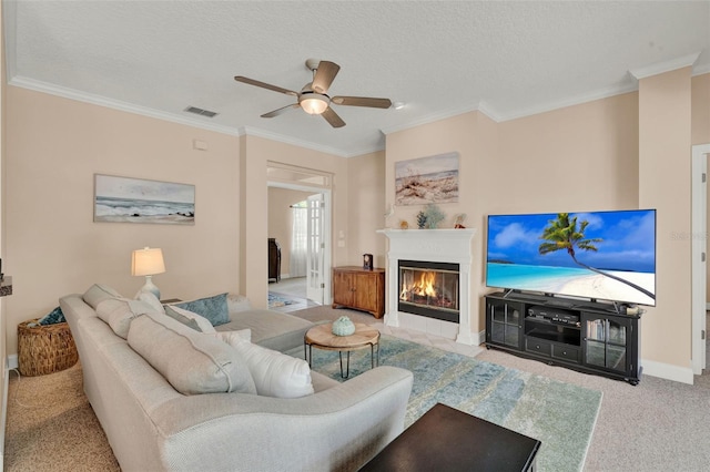 carpeted living room with ornamental molding, a ceiling fan, a tiled fireplace, baseboards, and a textured ceiling