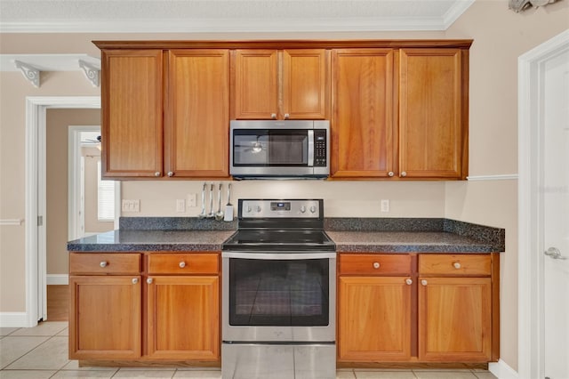 kitchen with stainless steel appliances, brown cabinets, crown molding, light tile patterned floors, and baseboards