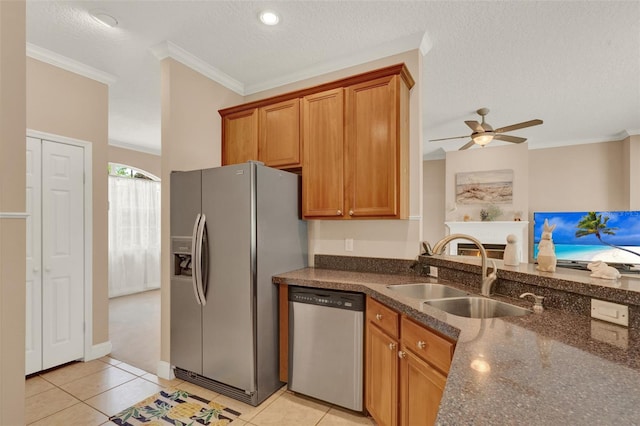 kitchen featuring appliances with stainless steel finishes, a sink, brown cabinetry, crown molding, and dark stone countertops