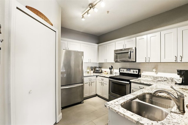 kitchen featuring tasteful backsplash, light stone countertops, a sink, stainless steel appliances, and white cabinetry