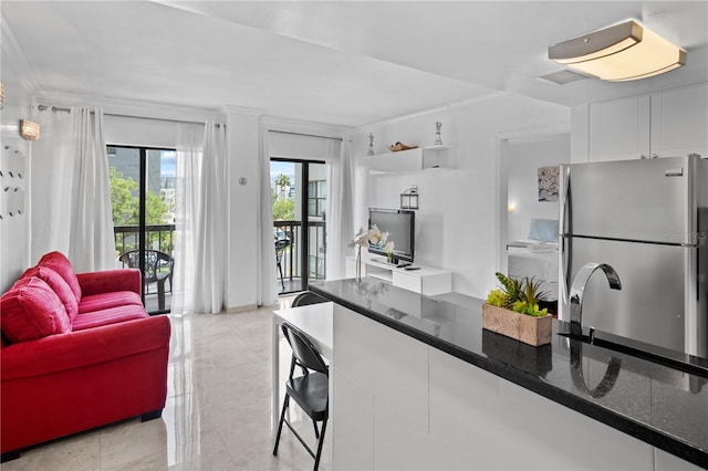 kitchen featuring dark stone counters, ornamental molding, freestanding refrigerator, and white cabinetry